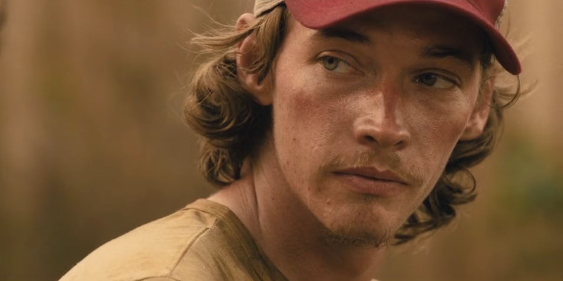 Close-up of Cooper Norris in Landman, wearing a red cap and looking intense while standing outdoors in the Texas oilfields.